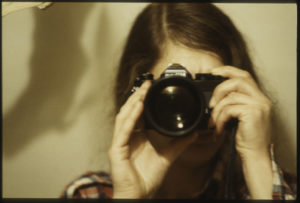 Selbstporträt einer jungen Frau mit Kamera und langen Haaren.
