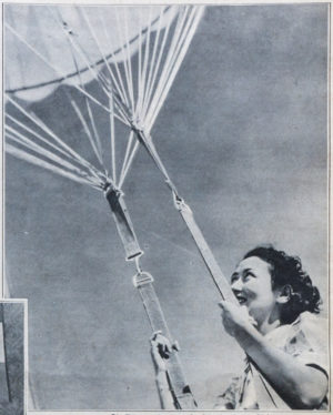 Eine lächelnde Frau mit welligen Haaren hält sich an den Seilen eines Fallschirms fest.