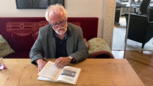 Der Historiker Gerhard Paul sitzt auf einer roten Couch und Blättert in einem Buch.