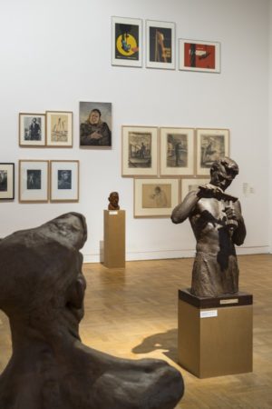 Ausstellungsraum in einem Museum mit Skulpturen im Vordergrund und Bildern an der Wand.