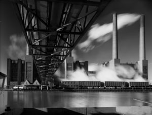 Bild von der Unterseite einer Brücke mit Fabrik im Hintergrund.