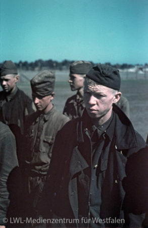 Vier Männer stehen mit düsteren Blicken in einem Feld.