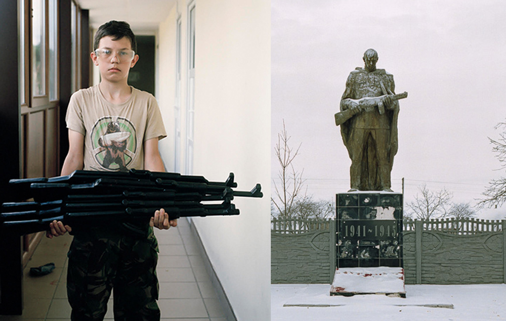 Rechts steht ein Kind in Camouflage-Hose mit langen Gewehren in den Händen, rechts die Statue eines Soldaten mit Gewehr im Schnee.
