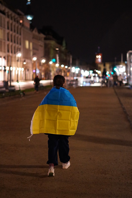 Eine Frau trägt die ukrainische Fahne um sich auf dem Rücken.