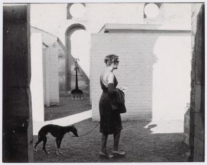 Eine Frau mit einem Hund vor einer Mauer, schwarz-weiß.
