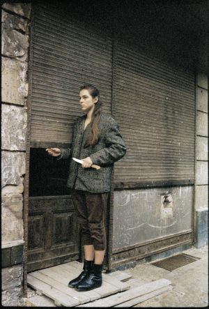 Eine Frau steht vor einem Eingang mit heruntergezogenen Rollläden.