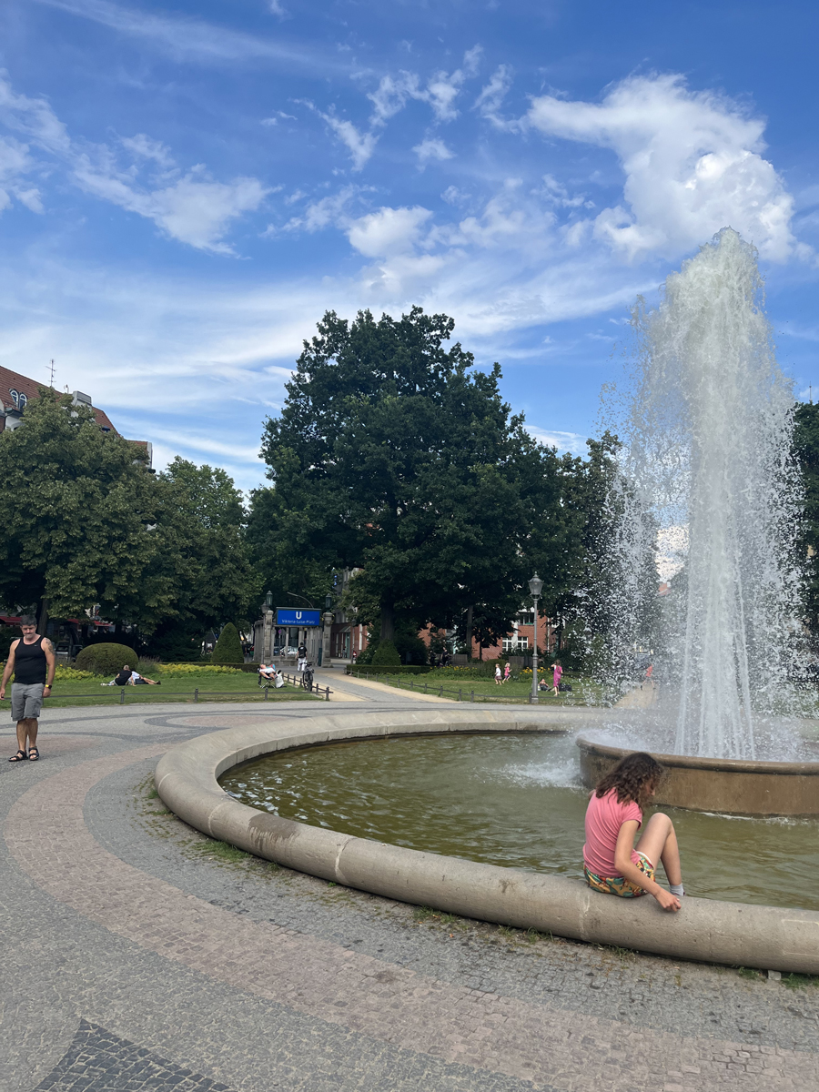 Ein Springbrunnen in einem Park, auf dessen Rand ein Kind sitzt.