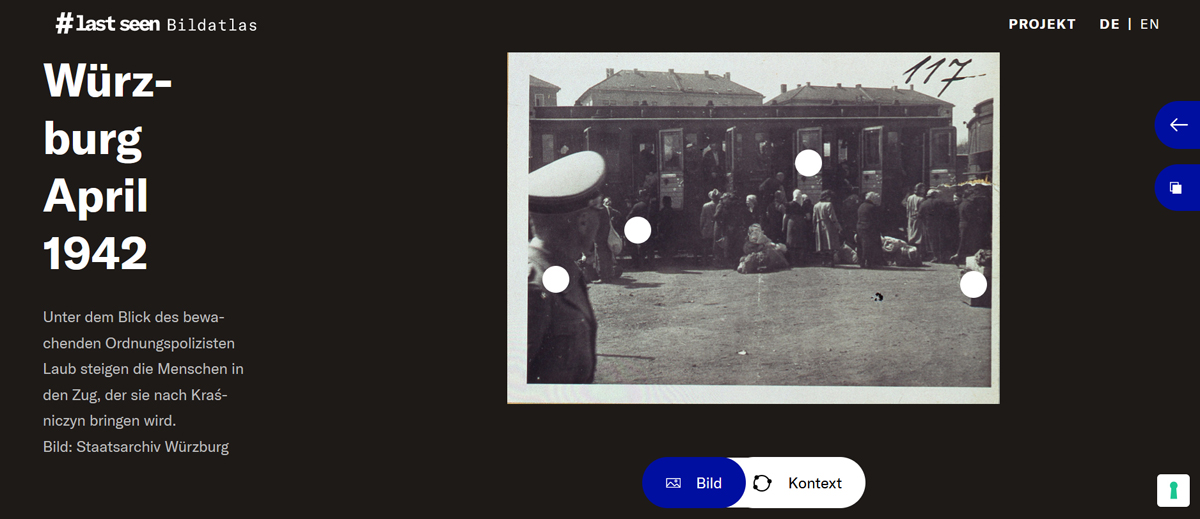 Screenshot: auf der rechten Seite eine Fotografie von einem Bahnsteig: Menschen steigen mit Gepäck in einen Zug, vorne links ist ein Mann in Uniform zu sehen. Links die Schrift auf schwarzem Grund: „Würzburg April 1942“ sowie die Beschreibung der Fotografie und die Seitennavigation.