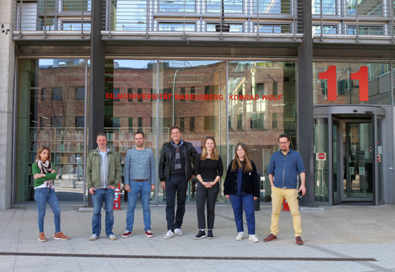 Sieben Personen (drei Frauen und vier Männer) stehen vor dem gläsernen Eingang der Filmhochschule Babelsberg.