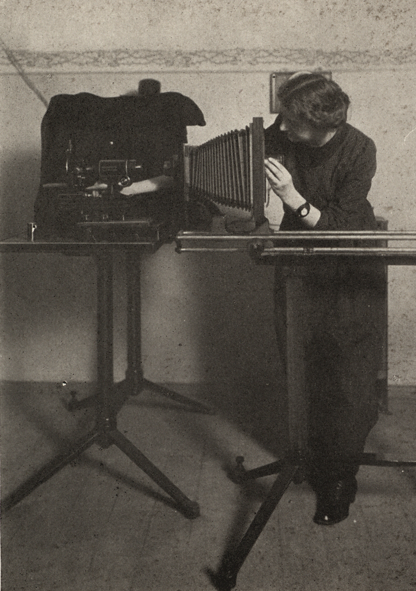 Eine junge Frau in einem langen schwarzen Kleid macht ein Foto mit Hilfe eines Mikroskops.