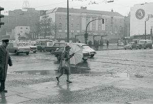 Schwarz-Weiß-Fotografie einer Frau mit Regenschirm an einer Straßenkreuzung