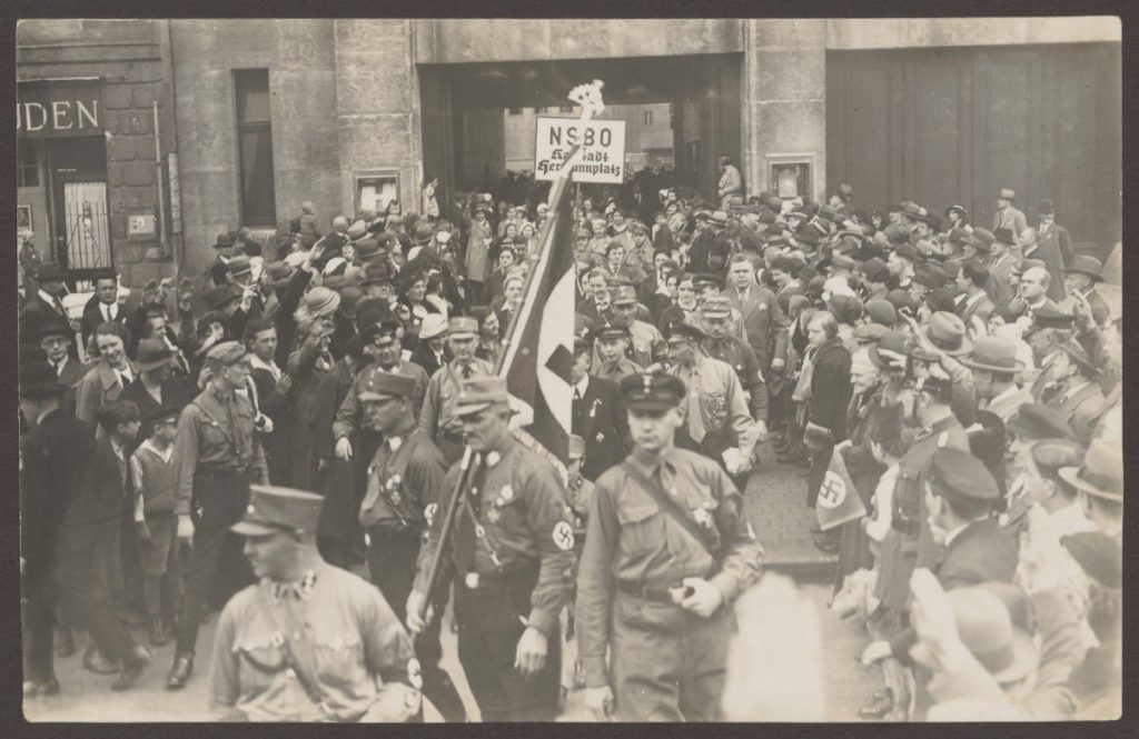 Foto von einem Zug von Männern in Uniform mit Zuschauern auf beiden Seiten