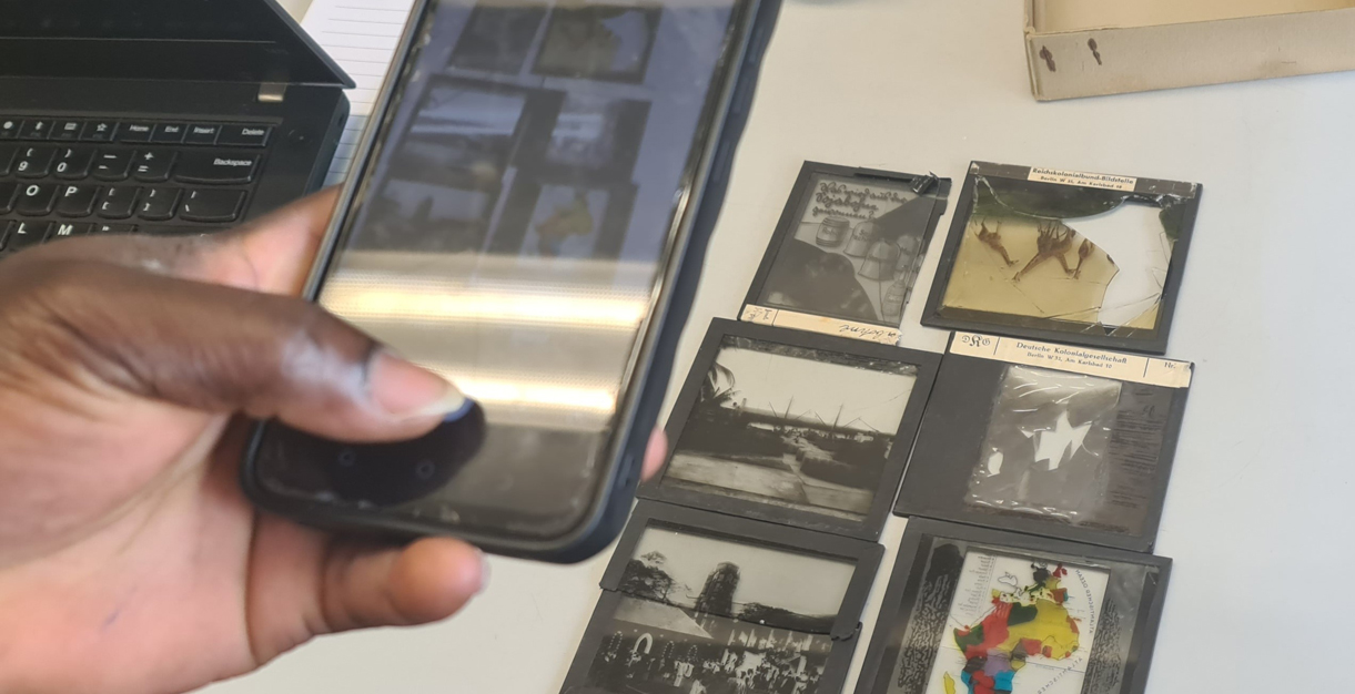 Foto von einer Hand mit Handy und Bildabzügen auf dem Tisch