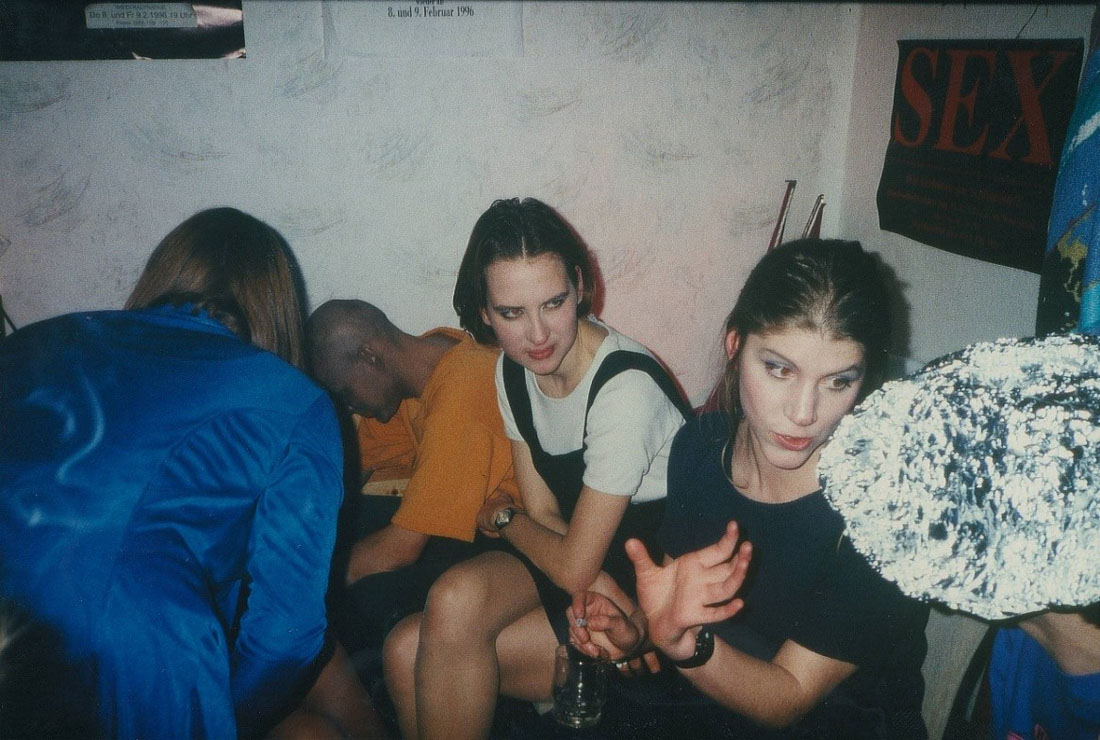 Farbfoto von Jugendlichen in einem Zimmer; im Vordergrund zwei junge Frauen