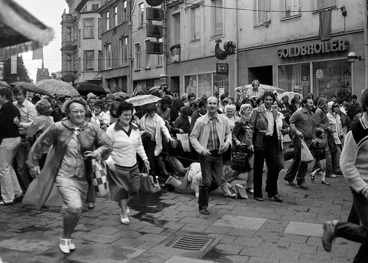 Schwarzweißfoto einer belebten Einkaufsstraße mit laufenden Menschen
