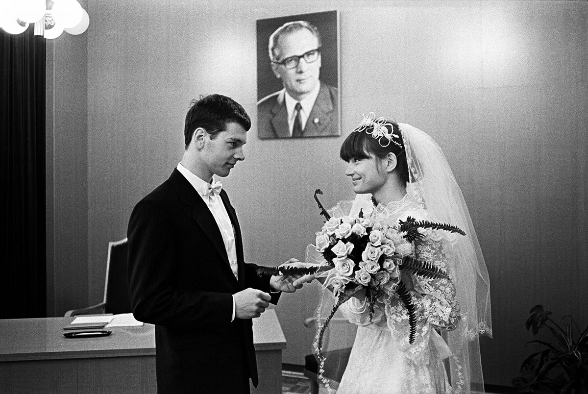 Ein Hochzeitspaar in einem Büro mit Bild von Erich Honecker an der Wand