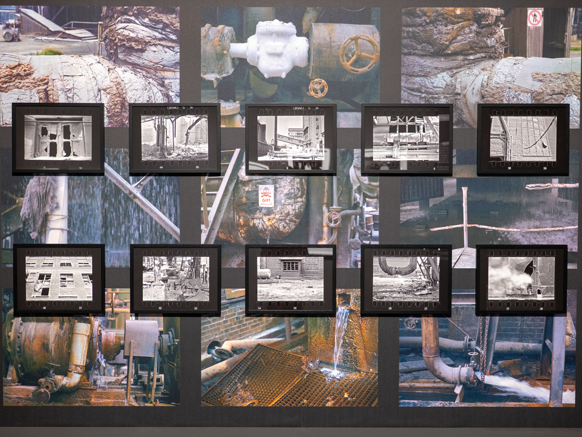 Farbfoto von Bildern auf einer Fototapete, die ein marodes Werk zeigt.