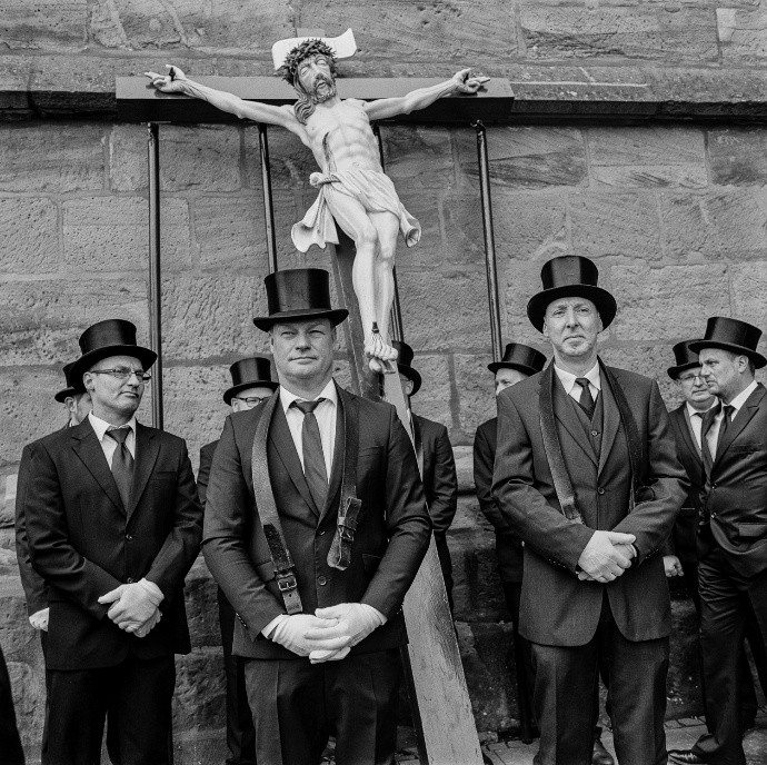 Schwarzweißfotografie von Männern in festlicher Kleidung mit Jesus-Statue