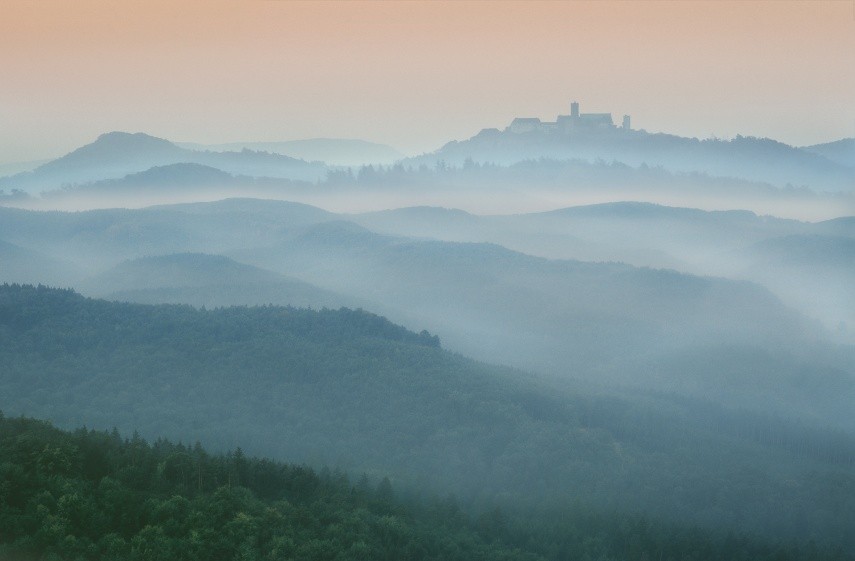 Farbfotografie von einer Burg und Hügeln im Nebel