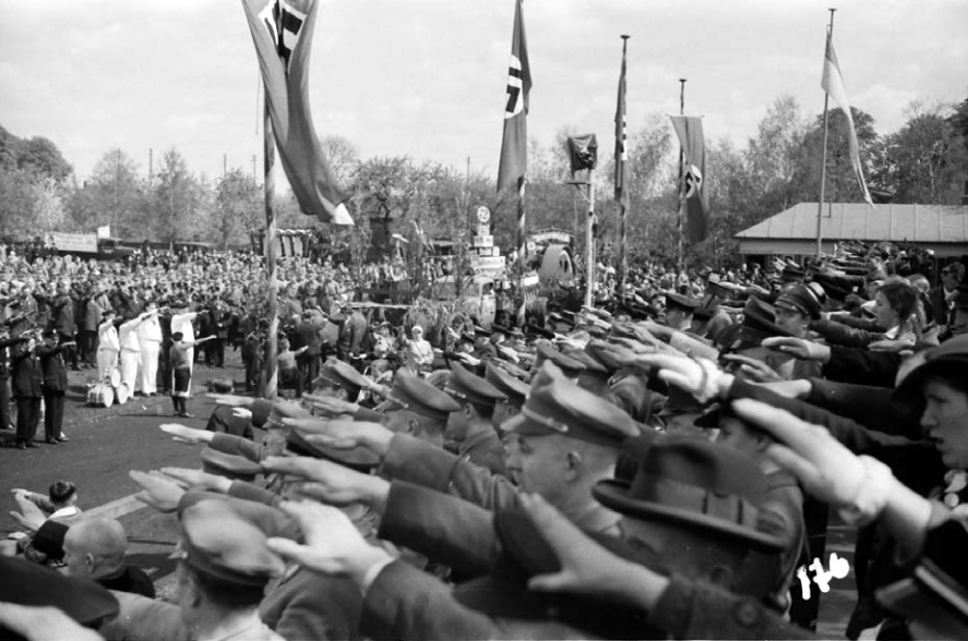 Schwarzweißfoto von einem Aufmarsch mit Fahnen und Zuschauern