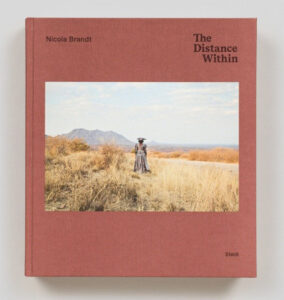 Roter Umschlag mit farbiger Fotografie einer Frau von hinten in einer Graslandschaft mit einem Berg im Hintergrund