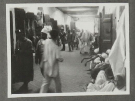 Verwackeltes Schwarzweißfoto von sitzenden und laufenden Menschen mit weißen Kopfbedeckungen