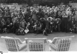 Schwarzweiß-Foto einer großen Zahl von Fotografen mit ihren Kameras vor drei Stühlen