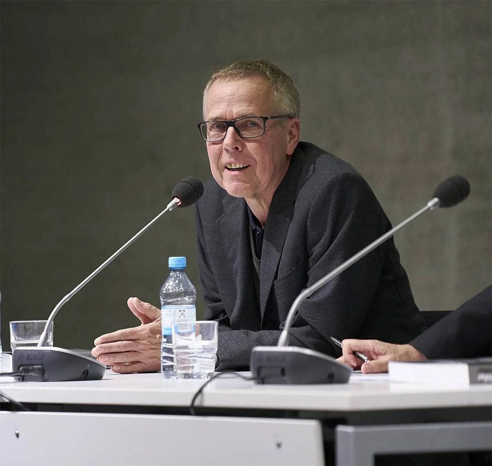 Farbfoto eines Mannes an einem Tisch sitzend mit Mikrofon