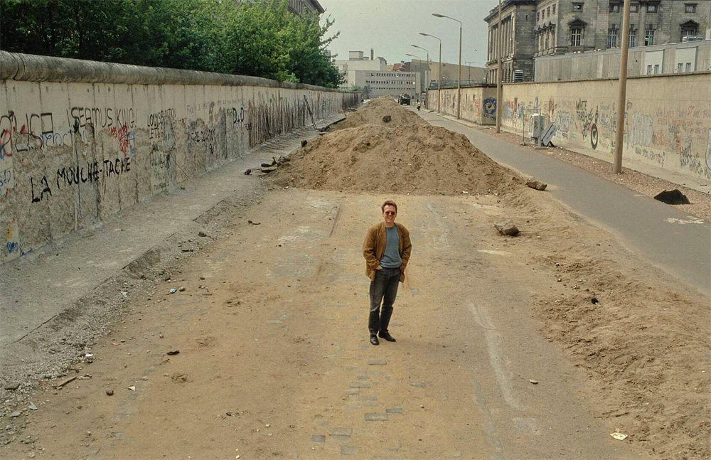 Farbfoto eines Mannes, der in einer aufgerissenen Straße steht, links und rechts Mauern.