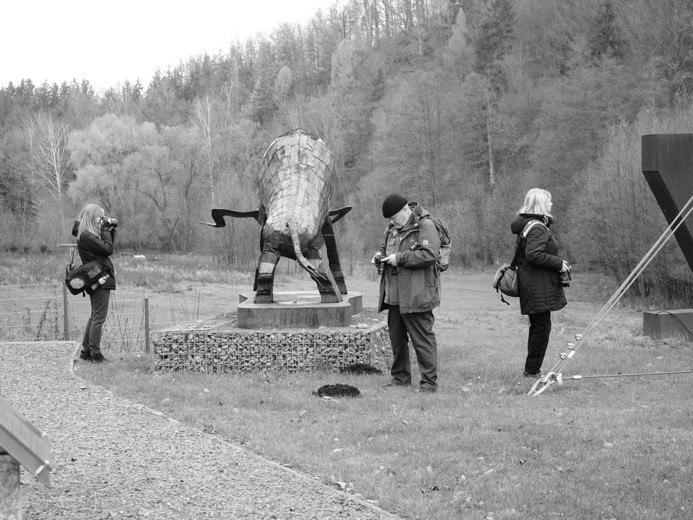 Schwarzweißfoto von drei Personen mit Fotoapparat in einer Landschaft mit Skulpturen