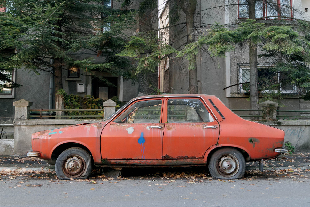 Farbfoto eines roten, mit Farbe besprühten Autos mit platten Reifen in einer Straße