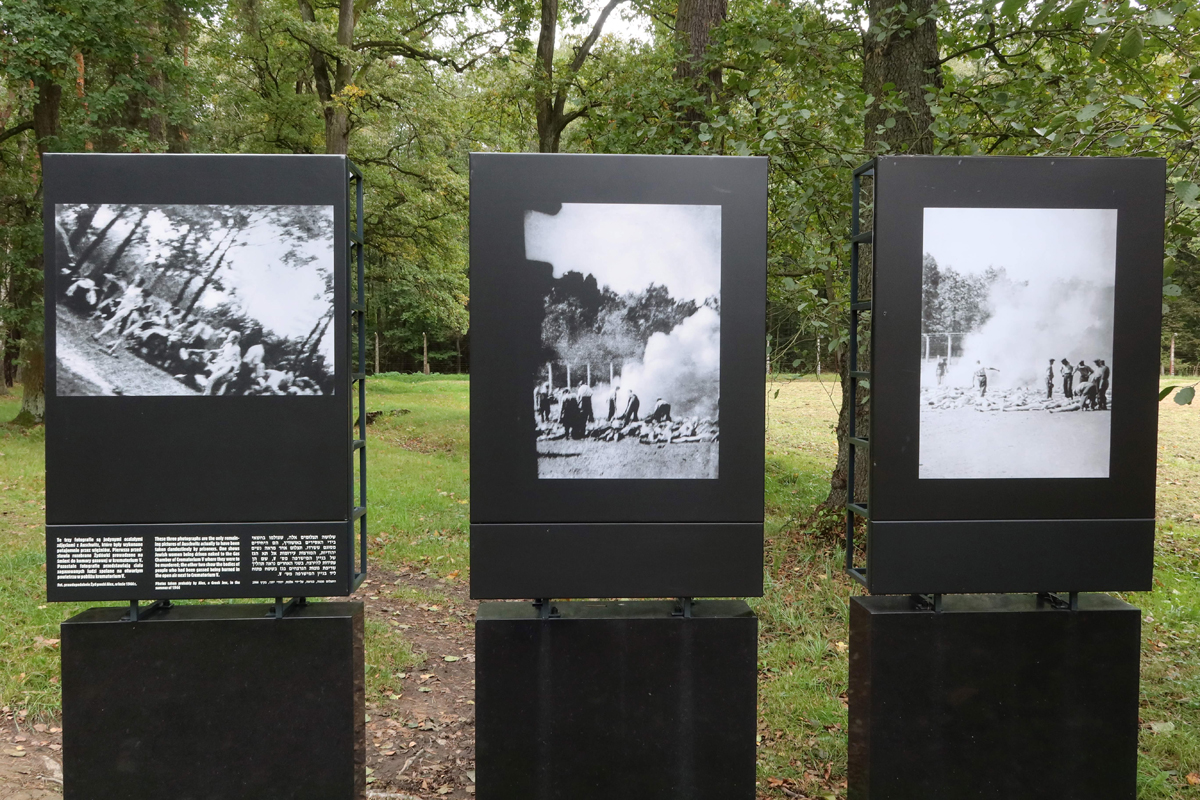 Farbfoto von drei Tafeln im Gelände mit drei Fotografien: Frauen im Wald und Leichen an der Verbrennungsgrube