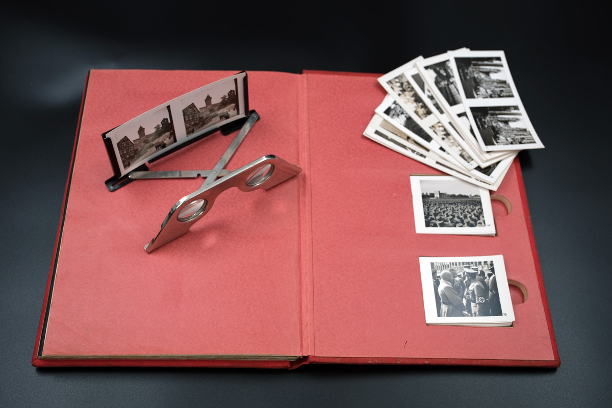 Farbfoto eines Albums mit rotem Einband und Stereobetrachter mit Stereobetrachter mit verschiedenen Stereoskopien
