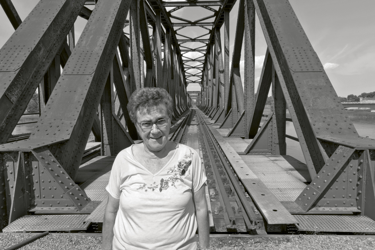 Schwarzweißfoto einer Frau vor einer Eisenbahnbrücke