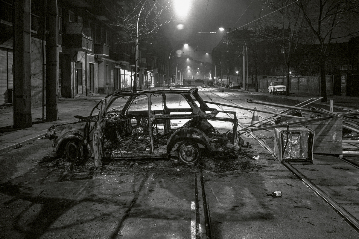 Schwarzweißfoto von einem ausgebrannten Auto in einer Straße nachts