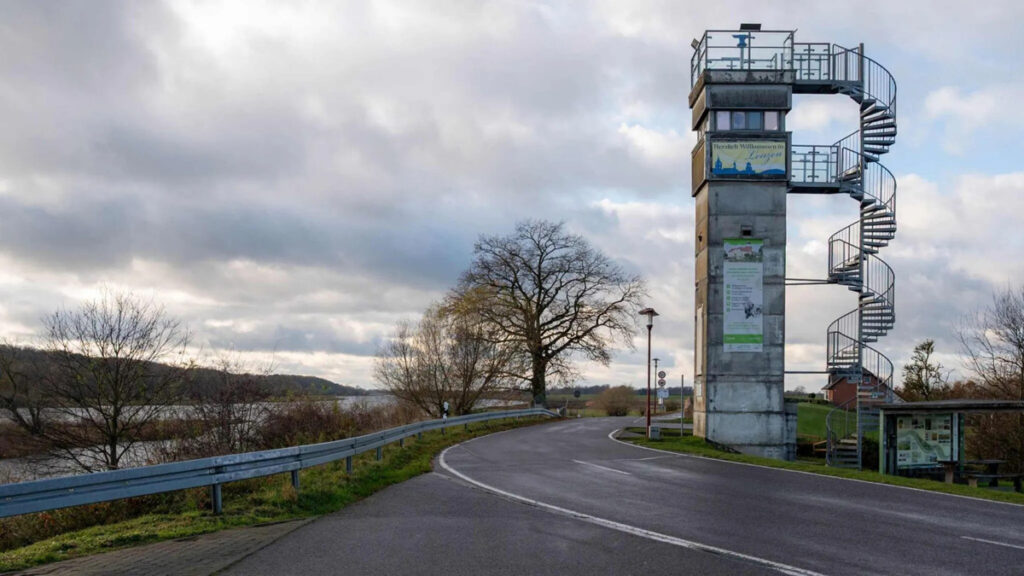 Farbfoto eines Flusses, einer Straße und eines Turms mit Außentreppe