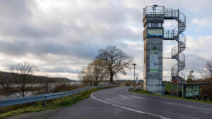 Farbfoto eines Flusses, einer Straße und eines Turms mit Außentreppe