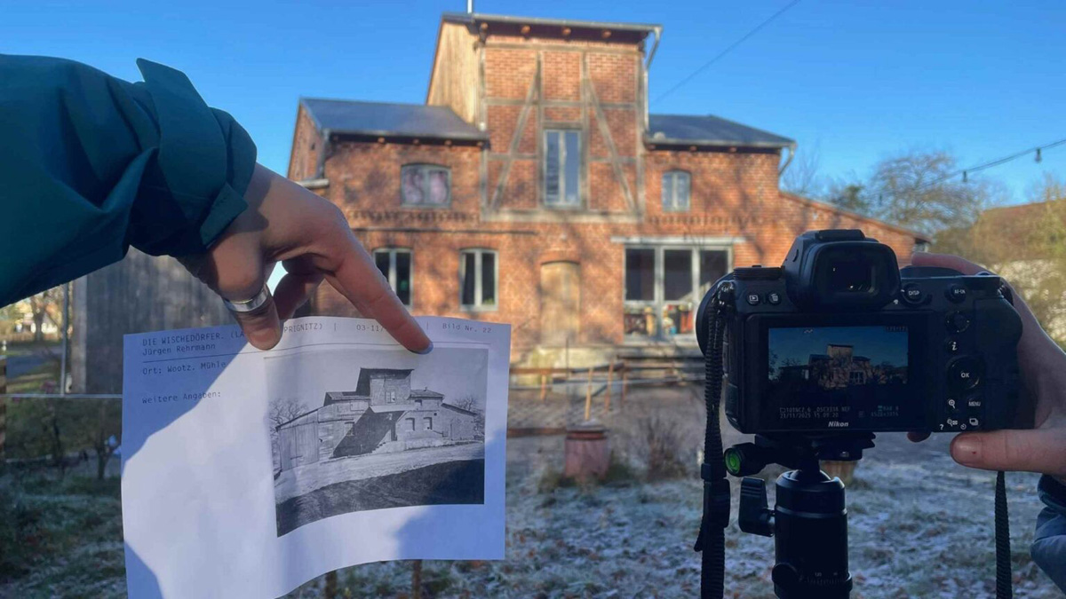 Farbfoto eines altes Ziegelhauses mit Kamera und alter Aufnahme davorgehalten